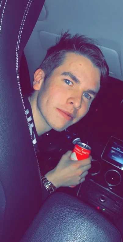 Paul smiling at the camera from his car, holding a can