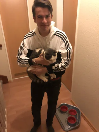 Paul standing in a hallway holding his cat in his arms