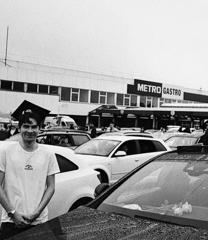 Black and white photo of Paul in a graduation cap, smiling in a car park